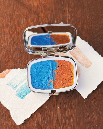 palette with blue and orange watercolour paint pans on a wooden surface