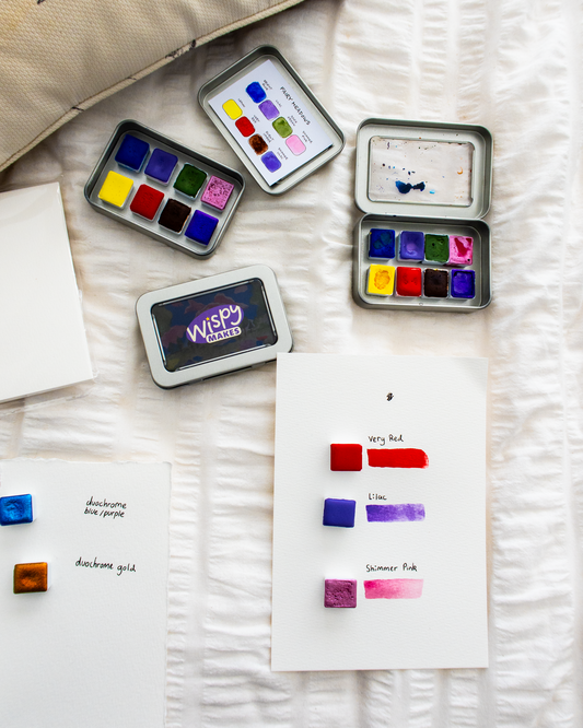 Set of watercolor pans and a color swatch on a textured surface