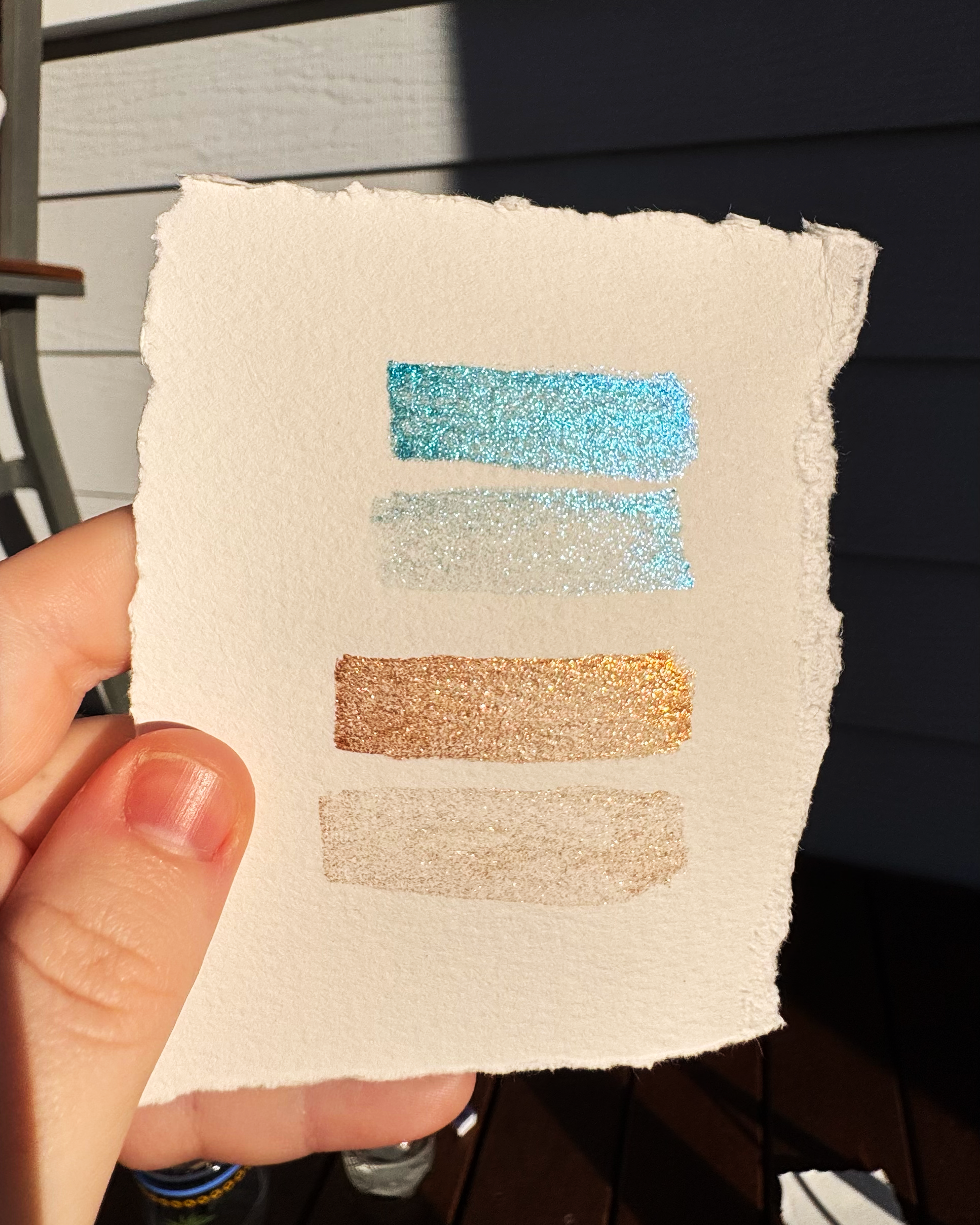 Hand holding a textured square with glittery color swatches against a neutral background