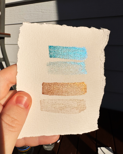 Hand holding a textured square with glittery color swatches against a neutral background