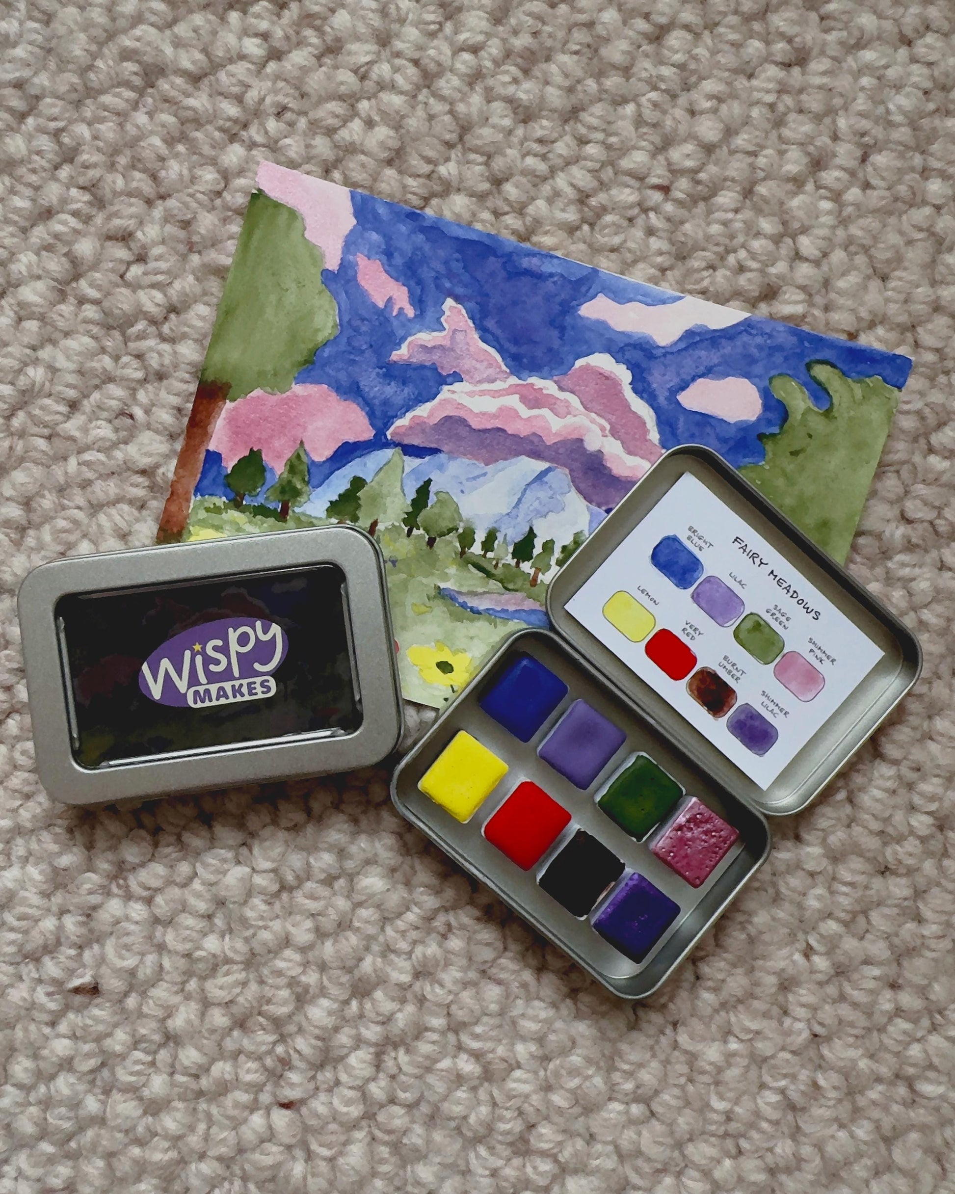 Watercolor paint set with a painted landscape on a carpeted floor